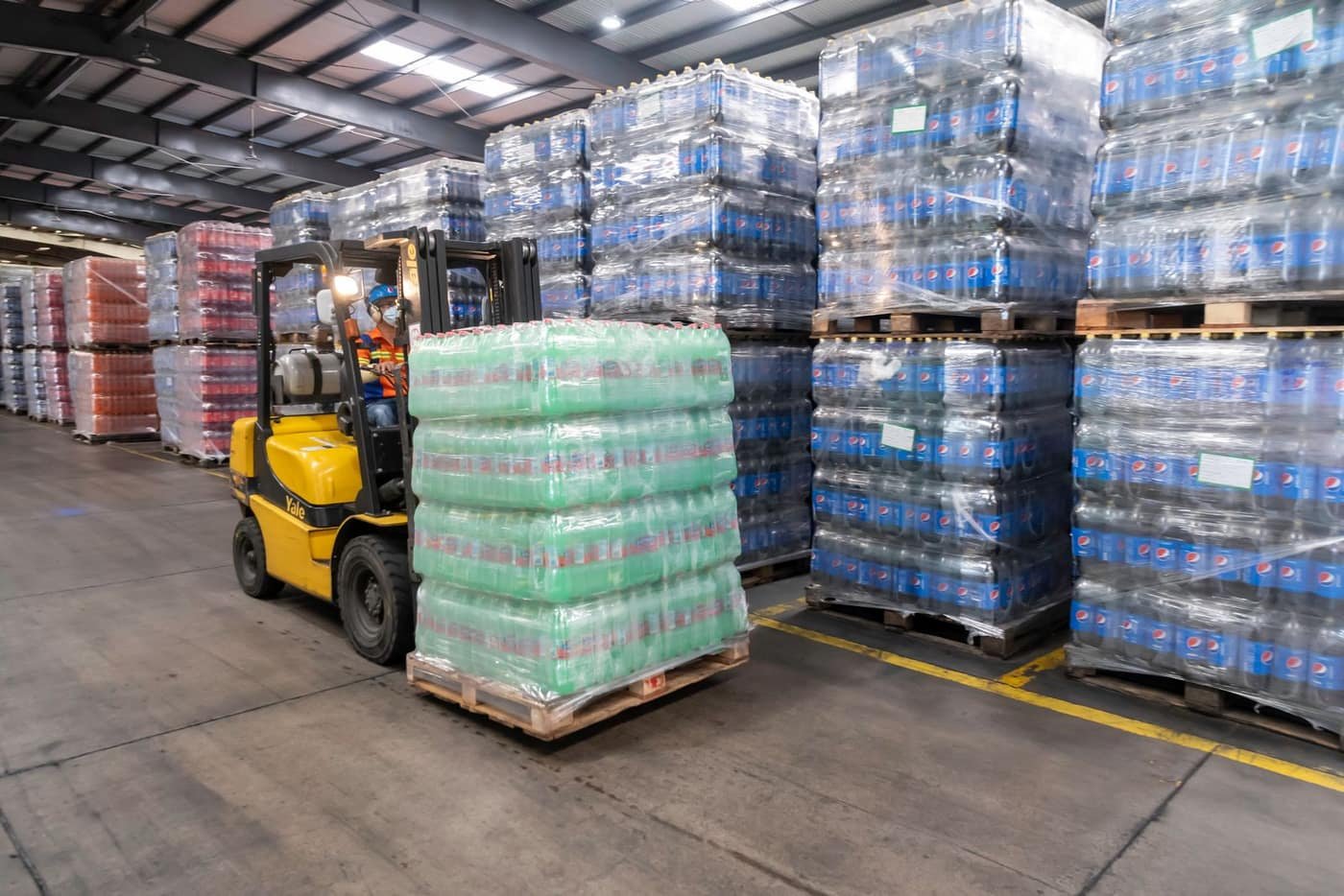 A forklift operator moving stacked pallets inside a warehouse